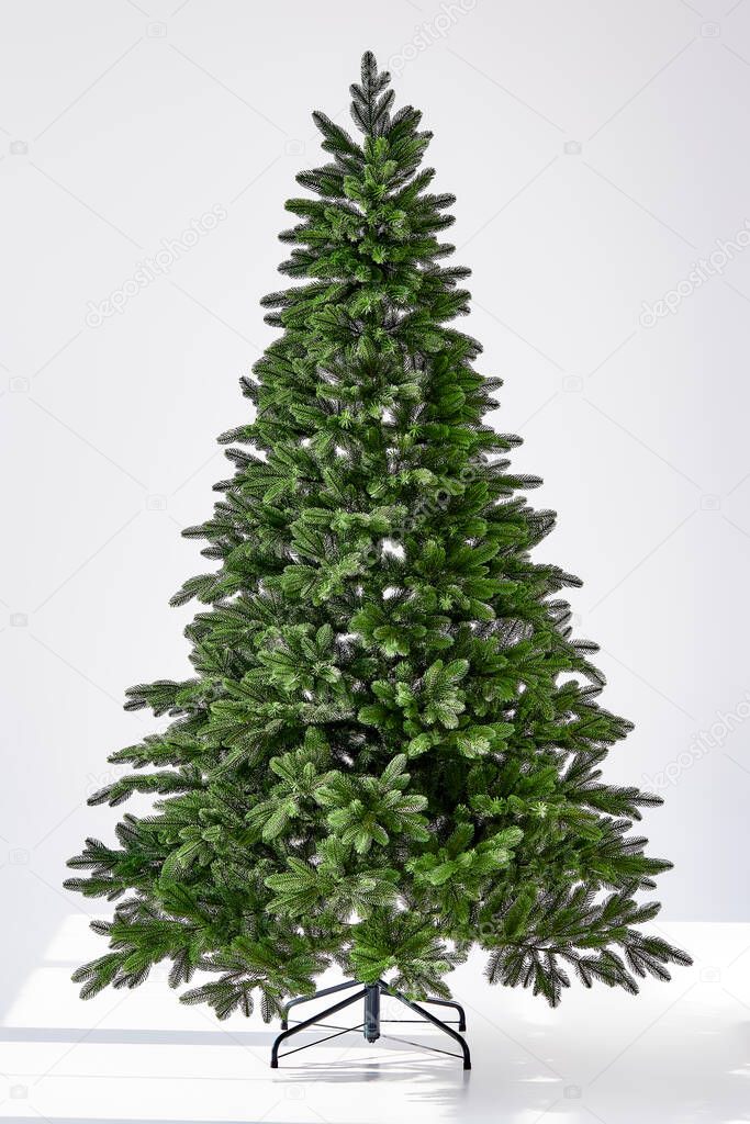 Artificial Christmas green tree without decorations on a metal stand isolated on a white background