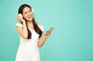 Genç Asyalı bir kadın en sevdiği müzik uygulamasını dinliyor. Kulaklığı cep telefonuyla yeşil arka planda izole edilmiş.