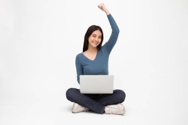 Yerde bacak bacak üstüne atmış, el pençe divan duran ve beyaz arka planda izole edilmiş dizüstü bilgisayar kullanan mutlu, genç Asyalı kadın.