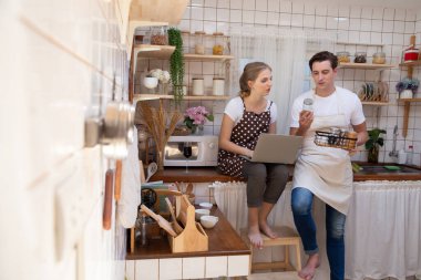 Kahvaltı hazırlayan genç bir çift ve mutfakta yemek pişirmek için menü arayan dizüstü bilgisayar kullanan bir kadın.