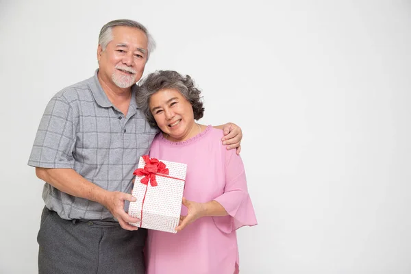 Senior Asian couple holding gift box with ribbon bow isolated on white background, Elderly Asian couple on valentine\'s day concept
