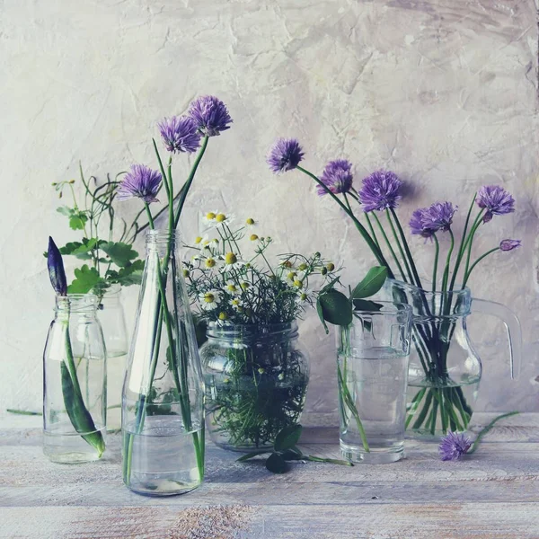Fresh spring flowers in transparent glass bottles with water on a wooden table, useful plants, essences