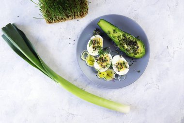 Avokado salatası, haşlanmış yumurta, pırasa, hardal, mikro yeşillik ve buğday tohumu tabakta hafif bir masada, sağlıklı beslenmek için doğal malzemeler.