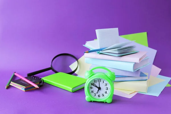放大镜 闹钟和桌上的记事本 与紫色底色的彩色纸 彩色纸 重返校园 度假等概念相对照 图库照片