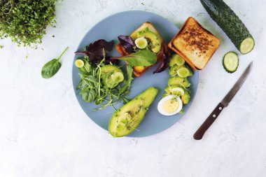 Avokado salatası, haşlanmış yumurta, pırasa, mikro yeşillikler lahanalar ve roka, bir tabakta hafif bir masada, üst manzara, düz, doğal malzemeler, sağlıklı yiyecekler.