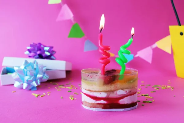 果物や燃えるキャンドルで飾られた誕生日ゼリーケーキ 休日の装飾 ピンクの背景の贈り物 コピースペース — ストック写真