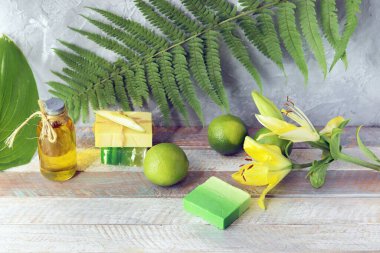 Doğal sabun, kireç, sarı zambak çiçeği, ahşap bir masada aromatik yağ, eğrelti otu yaprağı, spa, vücut bakımı ve rahatlaması için organik kozmetik ürünler.