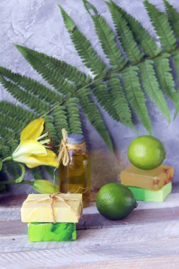 Doğal sabun, kireç, sarı zambak çiçeği, ahşap bir masada aromatik yağ, eğrelti otu yaprağı, spa, vücut bakımı ve rahatlaması için organik kozmetik ürünler.