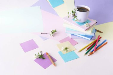 A stack of books, a cup of coffee, pencils, notepads and twigs of cherry blossoms on the table, against a background of colored paper in pastel colors, the concept of learning, education, back to school 