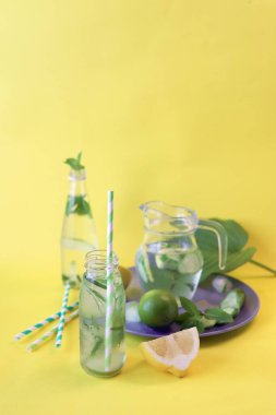 Limon dilimleri, limonlar, nane yaprakları, sarı arka planda cam şişeler, detoks su, limonata, doğal içecekler, ev yemeği.