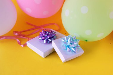 Gift boxes decorated with a bow of shiny ribbon, holiday balloons, bright yellow background, concept of congratulations, surprise, happy birthday