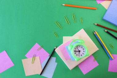 Stationery, alarm clock, books on a background of pastel colors of multi-colored paper, back to school, education, schoolchild study table, copy space, top view