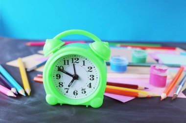Alarm clock on the table, against the background of multi-colored paper, books and stationery, back to school, education, table for schoolchildren
