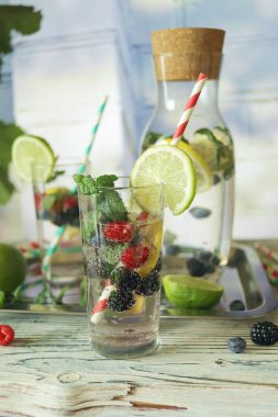Detox drink from berries, mint and citruses in glasses and a decanter, against the background of a light stone wall, seasonal drinks from organic natural ingredients