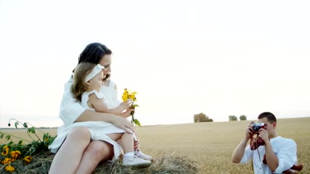 Aantrekkelijke moeder en kleine dochter zitten op hooiberg en poseren, vader neemt foto — Stockvideo
