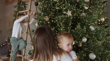 Mutlu anne ve küçük çocuklar yılbaşından önce Noel ağacını süsler.