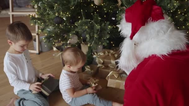 Due piccoli bambini felici ragazzi aprono la scatola dei regali di auguri di Capodanno data da Babbo Natale — Video Stock