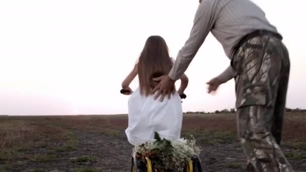 Bambina che impara ad andare in bicicletta con il nonno nel campo estivo al tramonto. — Video Stock