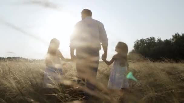 Kochający ojciec chodzi po żółtym polu z małymi córeczkami trzymającymi się za ręce. — Wideo stockowe