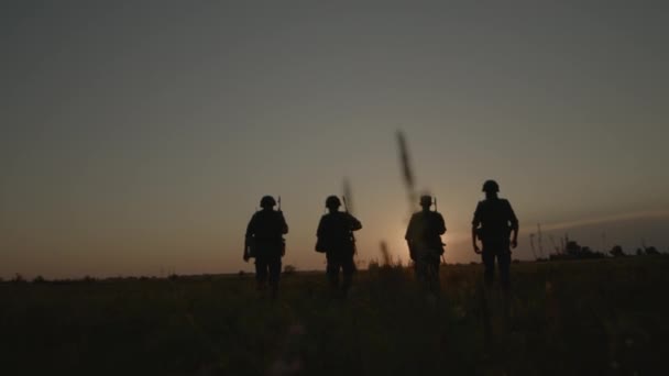 Silhouetten von Soldaten oder Offizieren mit Waffen in Tarnung, die bei Sonnenuntergang gehen — Stockvideo