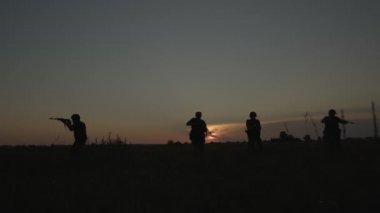 Kamuflaj kıyafetli askerler silahlarıyla sahada koşuyor ve nişan alıyorlar..