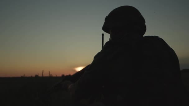 Infantryman in helmet with rifle aiming at hostile forces at sunset on field. — Stock Video