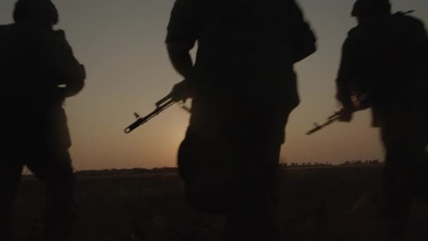 Silhouette di tre soldati con arma che corrono attraverso il campo al tramonto. — Video Stock