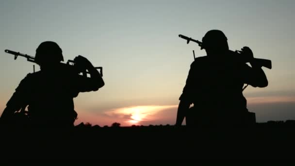 Два вооруженных человека с оружием идут по полю после боевой операции, вид сзади. — стоковое видео