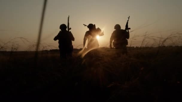 Two armed men with weapon walking across field after combat operation back view. — Stock Video