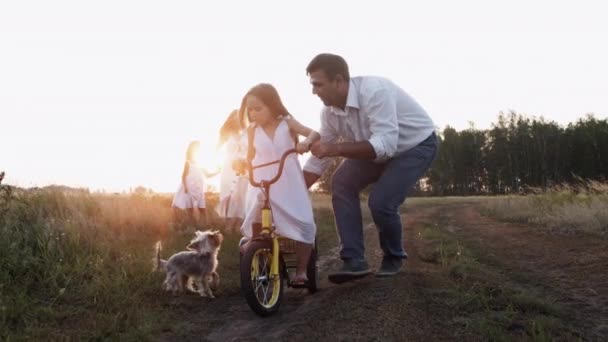 充满爱心的父亲 迷人的母亲和美丽的孩子们在暑假里的体育活动 可爱可爱的小狗追着可爱的小孩骑自行车跑 关心的爸爸帮助女儿 快乐的童年 — 图库视频影像