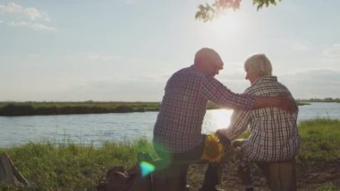 Happy smiling older couple embrace, talks sitting together on lake beach in sunshine outdoor. Spouse harmony, human idyllic and love, funny aged marriage, romantic date, family peaceful rest at nature