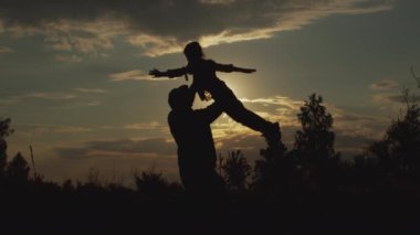 Silhouette of careful father circling, lifting little lovely daughter, together playing funny plane game at sunset outdoors. Carefree dream childhood, family life happiness, candid human relationship