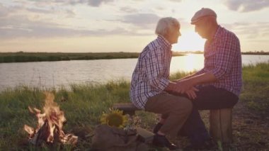 Happy affectionate elderly grandparents together hugging sitting at lake beach date at sunset close up outdoors. Carefree caressing love, calm tenderness, sensual cuddle and support of two old spouses