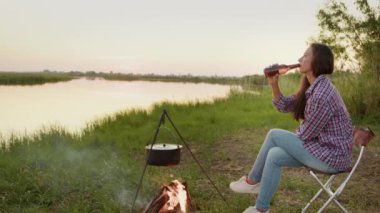 Adult awe woman does drink glass beer beverages, sitting in lotus position on boardwalk near serene water outdoors alone for emotional relief. Mental relax for healthy body, deep enjoy, wellness