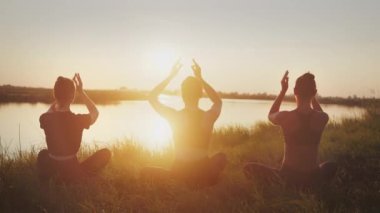 Atletik kadın grubunun silueti, gün batımında sakin suyun yanında tahta kaldırımda durarak esneme egzersizi yapıyorlar. Sağlıklı yaşam tarzı, vücut ısısı, fiziksel rahatlama için aktif vücut bakımı.