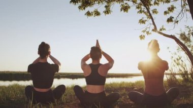 Silhouette of diverse group of three female together going, sitting in lotus, namaste positions on seaside boardwalk outdoors. Do yoga exercise, awe meditation for control mind, mental health, harmony