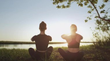 Birlikte jimnastik yapan iki düşünceli kız, dışarıda, deniz kenarında oturarak yoga egzersizi yapıyorlar. Çocuklar sağlıklı vücut için spor yapar, esneklik, zihin rahatlığı, uyum.