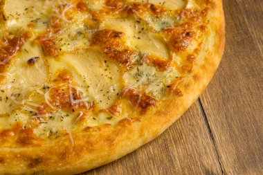 Ahşap arka planda peynirli ve armutlu fırında pizza.