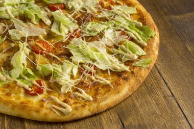 Peynirli pizza, marul ve ahşap arka planda vişneli domates.