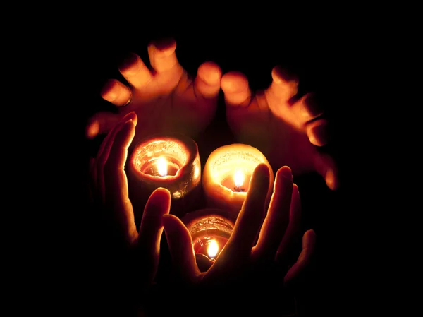 Burning candles and hands in darkness — Stock Photo, Image