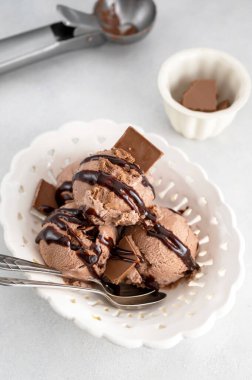 Chocolate ice cream balls, scoops with chocolate syrup in bowl on gray background, summer treat