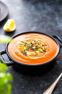 Siyah kasede taze bitkilerle domates çorbası. Karanlık arka plan. Vejetaryen kremalı çorba.