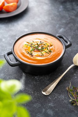 Siyah kasede taze bitkilerle domates çorbası. Karanlık arka plan. Vejetaryen kremalı çorba.