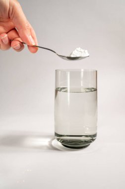 Kadın bej arka plandaki bir bardak suya kolajen tozu ya da protein döker. Sağlıklı ve yaşlanmayı önleyici bir ilave. Boşluğu kopyala