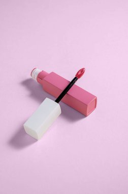 Pink liquid lipstick and applicator brush with open tube. Makeup cosmetic product. Pink background