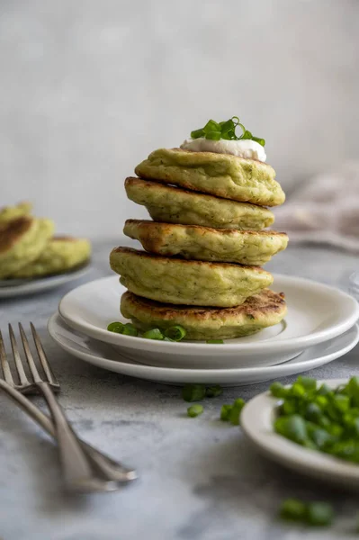 Zucchini fritters, stack of vegetarian zucchini pancakes, with fresh herbs and sour cream