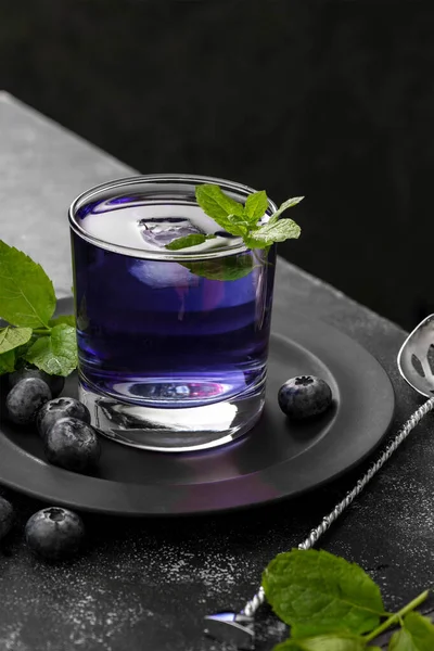 Colorful purple blueberry cocktail with fresh berries and mint. Dark, moody background