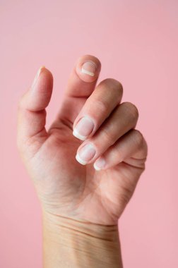 Doğal sağlıklı tırnakları olan bir kadın eli. Güzellik, el ve cilt bakımı kavramı. Pembe arkaplan.