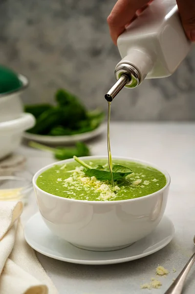 Spinach soup. Pouring olive oil in bowl of green creamy, vegan creamy soup on bright background.