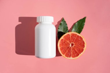 Doğal gıda takviyesi hapları, vitaminli beyaz plastik şişe, pembe arka plan ve gölgeli güneş ışığı.